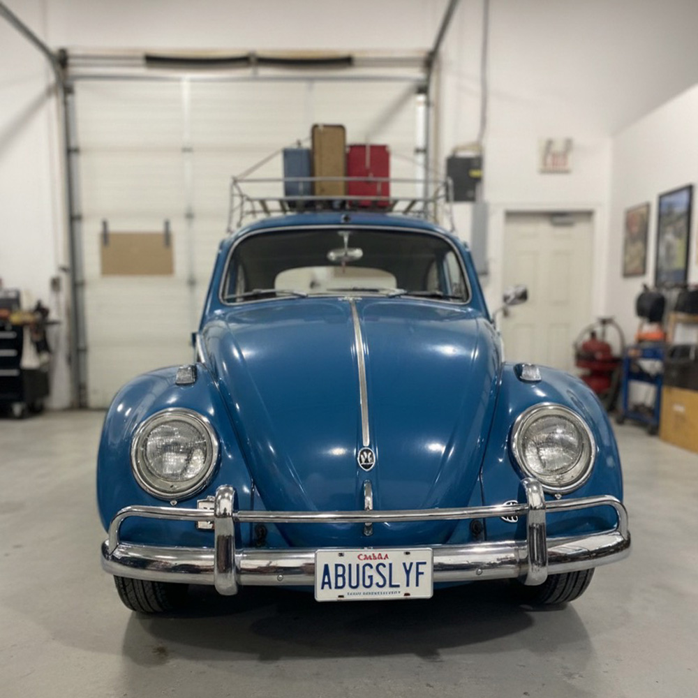 Blue VW Beetle parked in garage with vintage suitcases on roof rack and Canadian plate