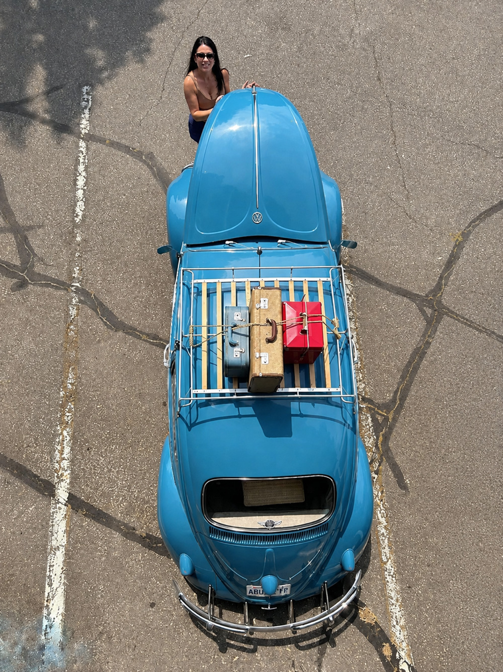 Overhead view of blue VW Beetle with roof-rack luggage and the owner standing near the front