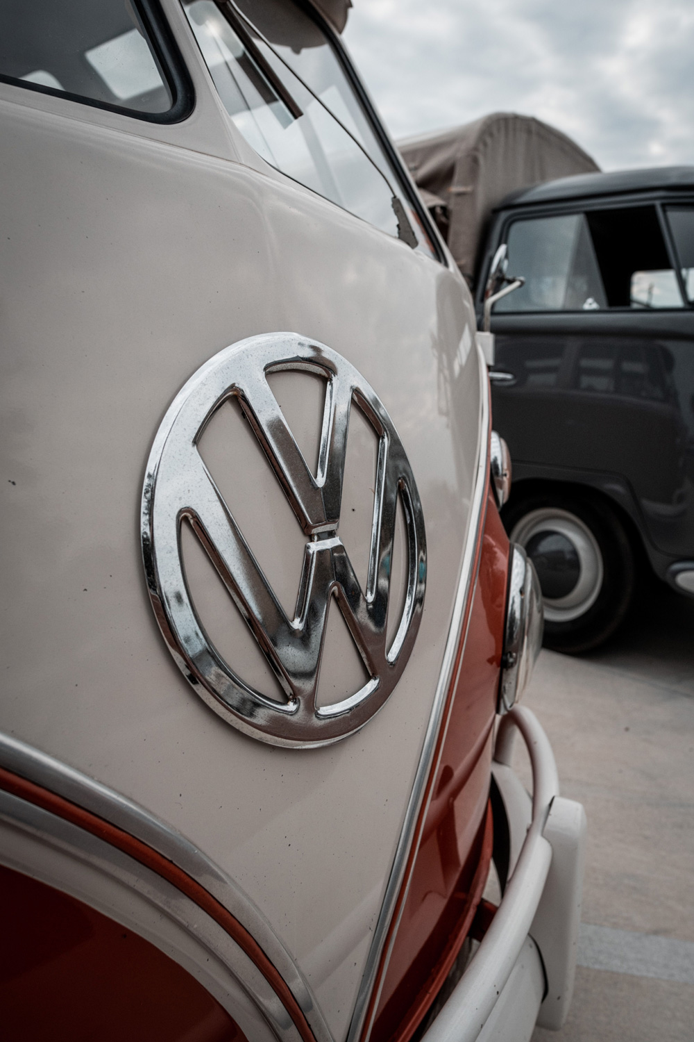 Close front view of a cream and red VW Type 2 at a 2026 Volkswagen gathering with another van behind it