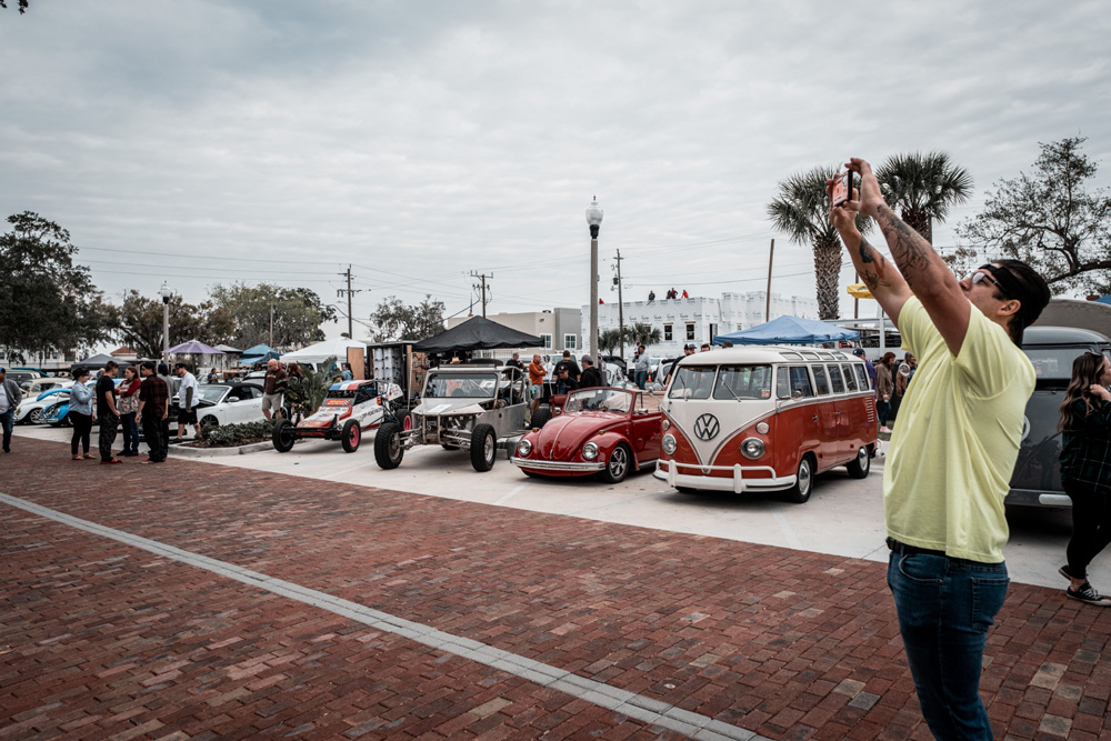 Classic VW vans, Beetles, and a dune buggy at a busy outdoor 2026 Volkswagen festival
