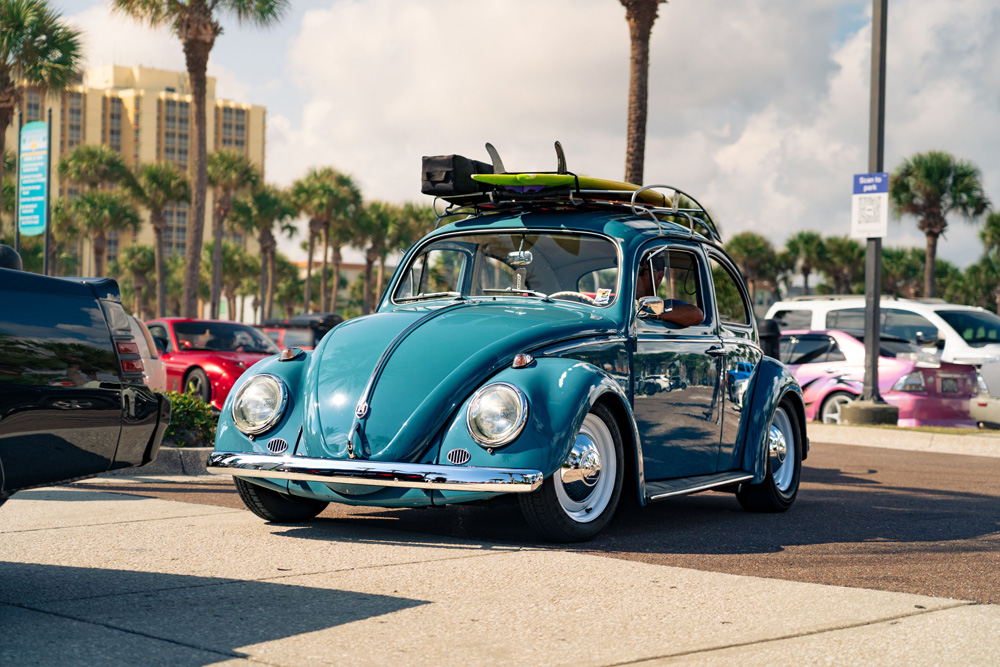 Turquoise Volkswagen Beetle with surfboard on the roof at a sunny 2026 VW beachside event