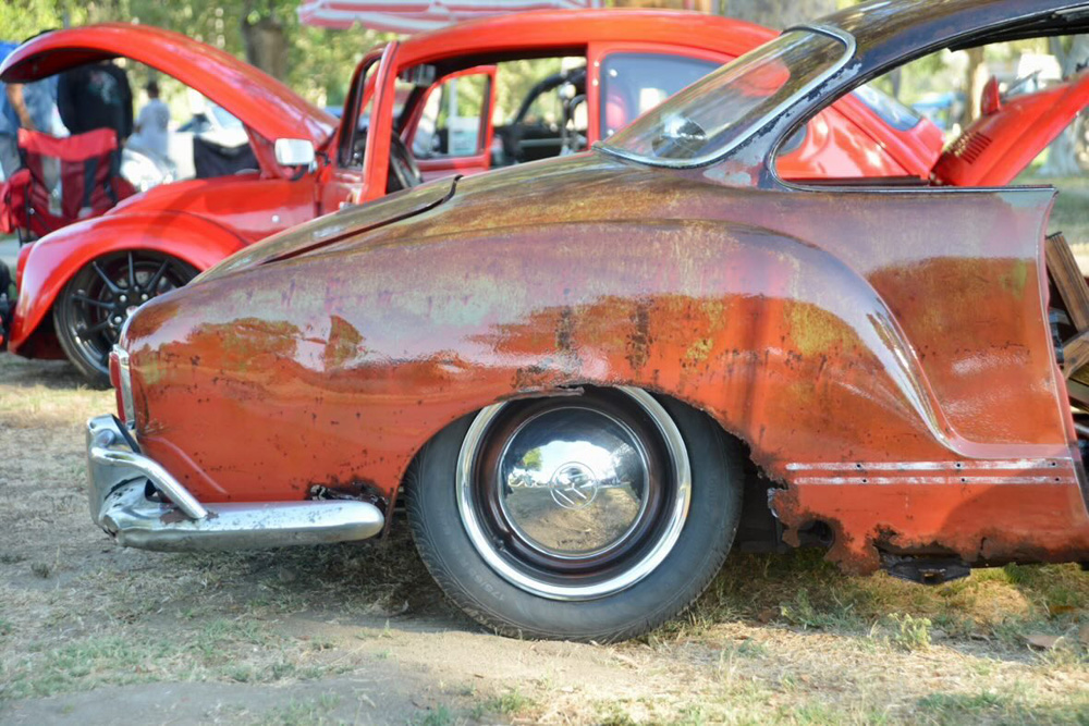Close up of a patina Karmann Ghia with chrome bumper and a red Beetle in the background at the El Prado VW Show & Shine