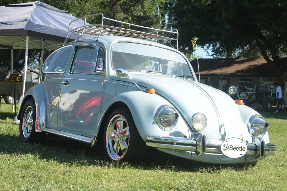 Light blue Volkswagen Beetle with chrome bumpers and roof rack parked on the grass at the El Prado VW Show & Shine